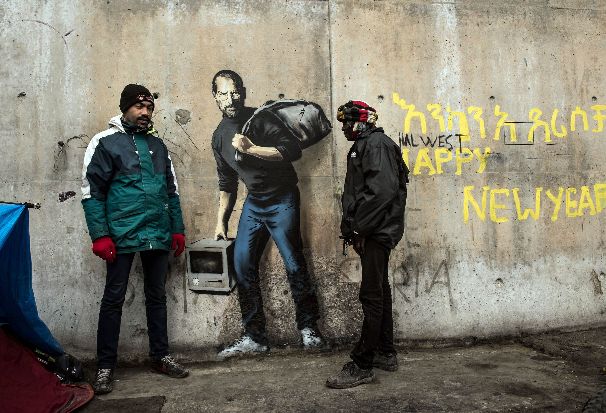 ستيف جونز المهاجر واللاجئ الكوني على حائط مخيم عشوائي في كاليه-فرنسا بريشة فنان الغرافيتي الشهير بانكسي